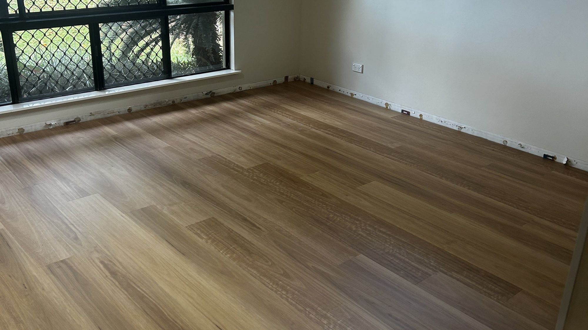 An empty room with new timber floorboards and windows looking out to the garden