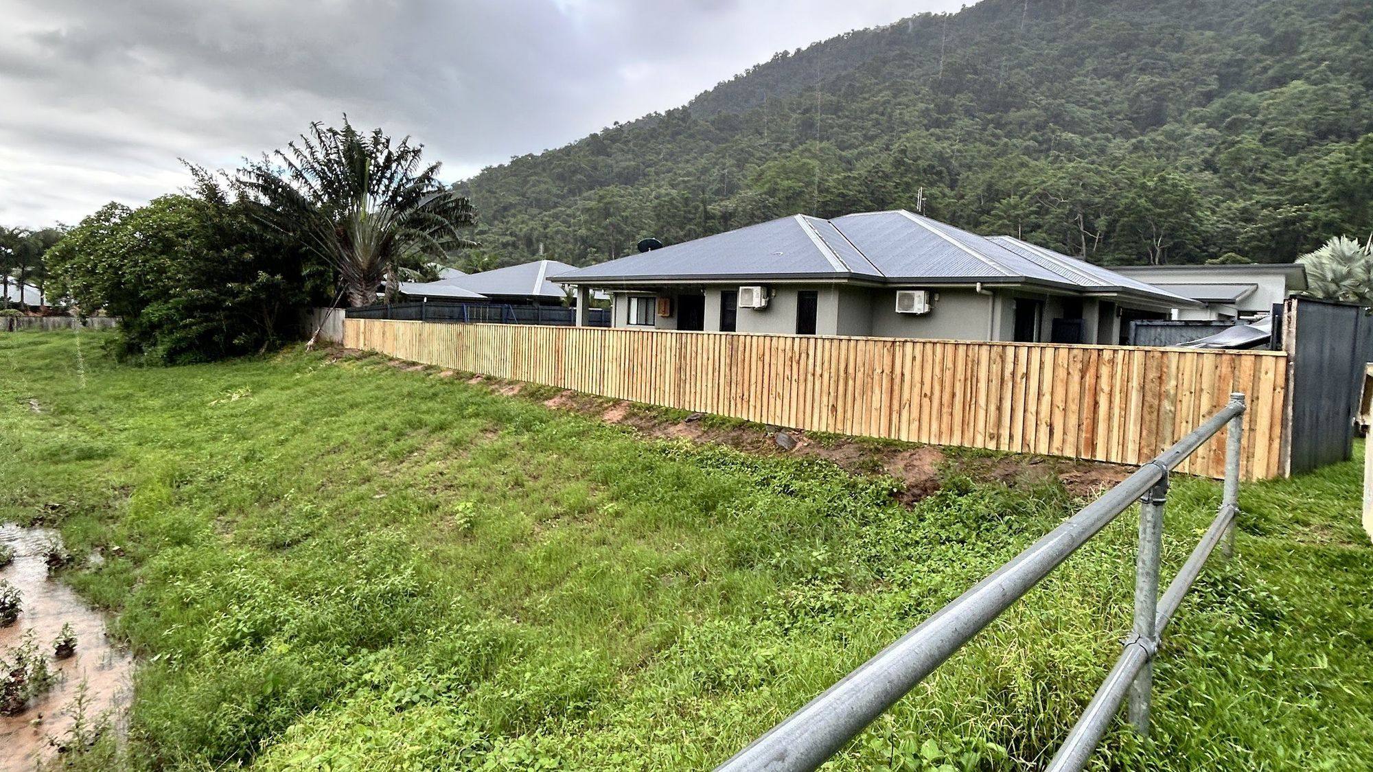 A new timber paling fence running along a green hillside under a heavy sky