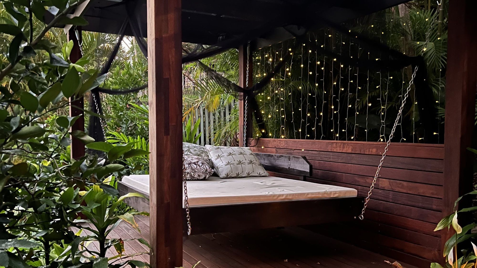 A hardwood pergola and daybed lit with string lights and lanterns at dusk