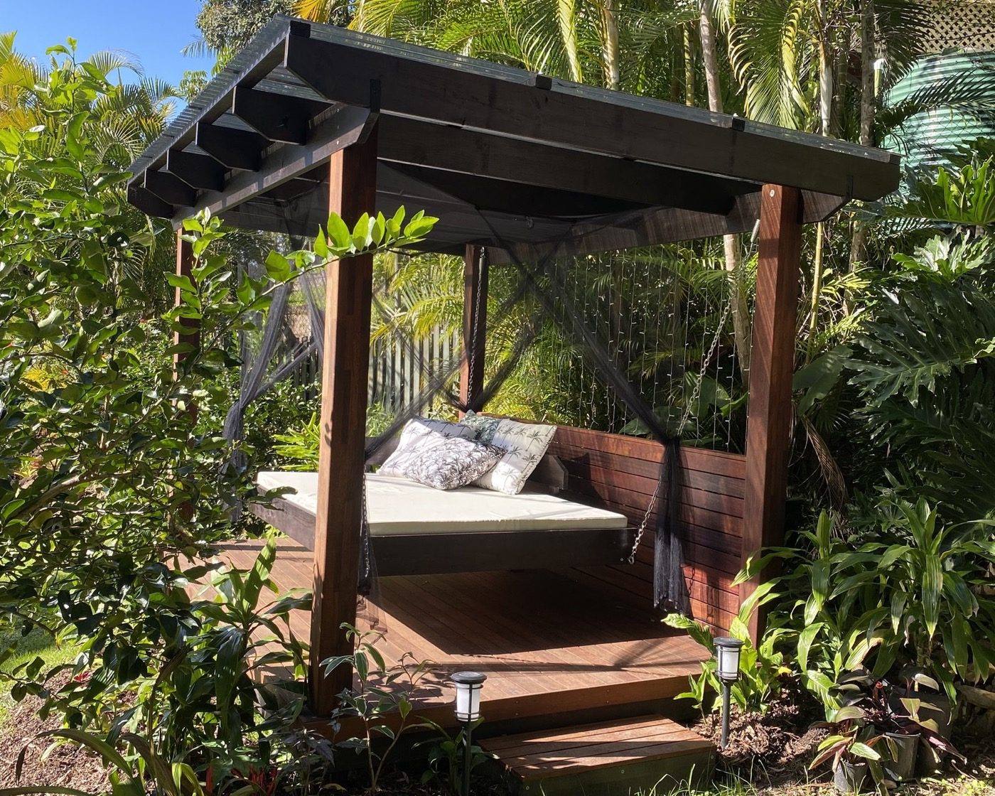 A hardwood pergola with a slatted screen and a hanging daybed under a corrugated roof