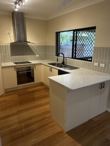 A kitchen with a rangehood and stone benchtop above new timber floorboards