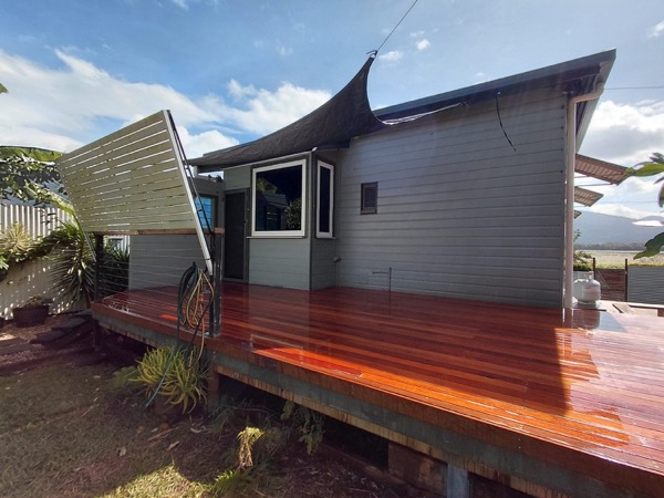 A merbau deck and bench seat wrapping a weatherboard home under a shade sail