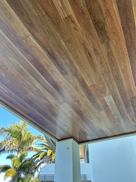 A hardwood-lined eave running out to a blue sky and palm fronds